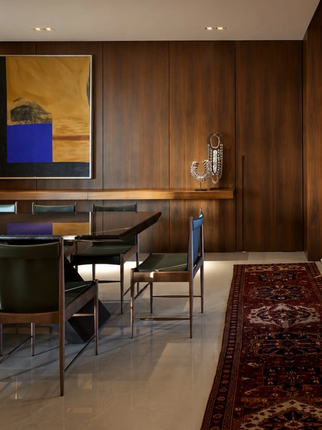Sala de jantar com painel de nogueira, mesa escura, cadeiras em couro verde e tapete persa